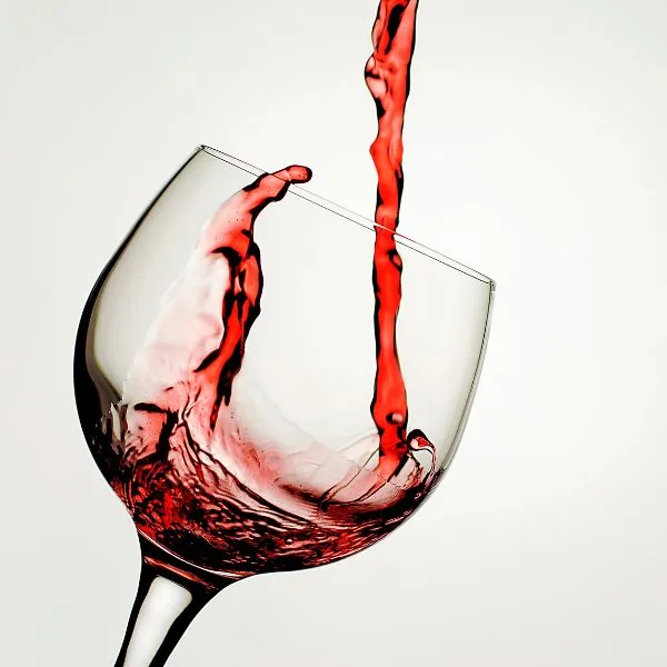 Red wine streaming into a tilted glass, splashing up the bowl against a white background