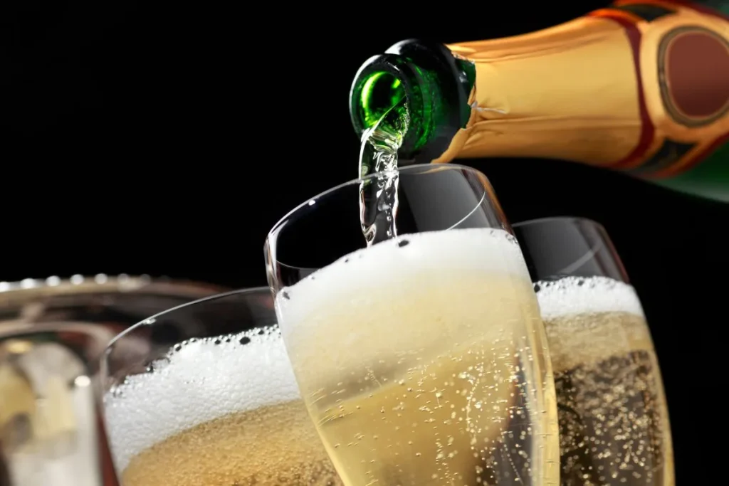Sparkling wine poured from a gold foil bottle into flutes with thick foam