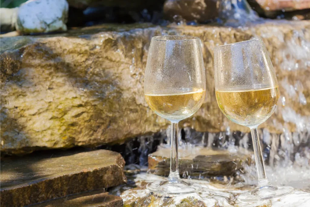 Two glasses of chilled white wine with condensation resting on wet rocks beside running water