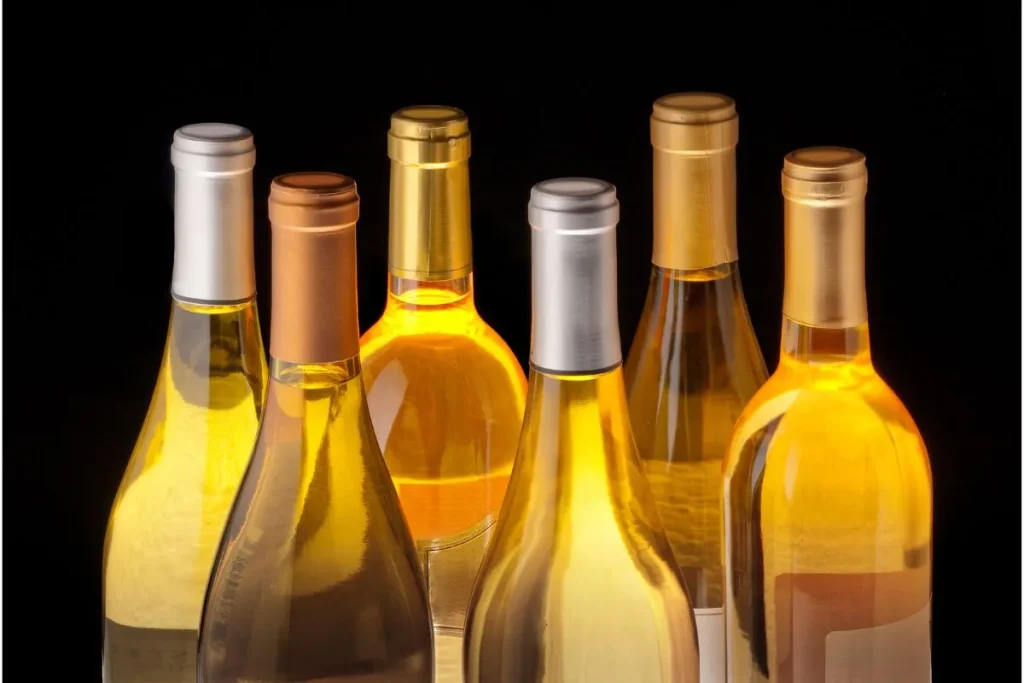 Six backlit bottles of white wine with foil capsules against a black background