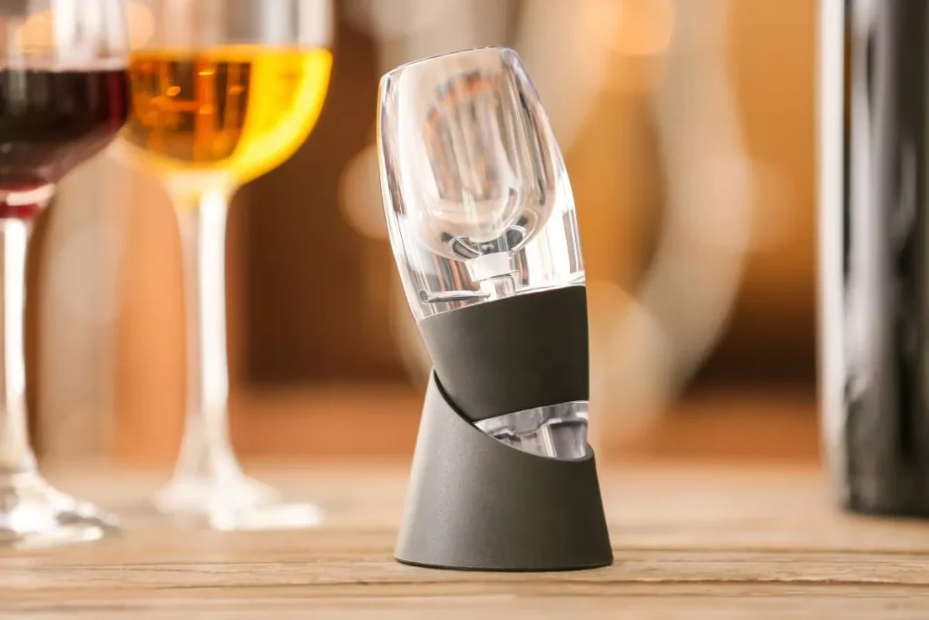 Clear wine aerator in a black stand on a wooden table beside glasses of red and white wine