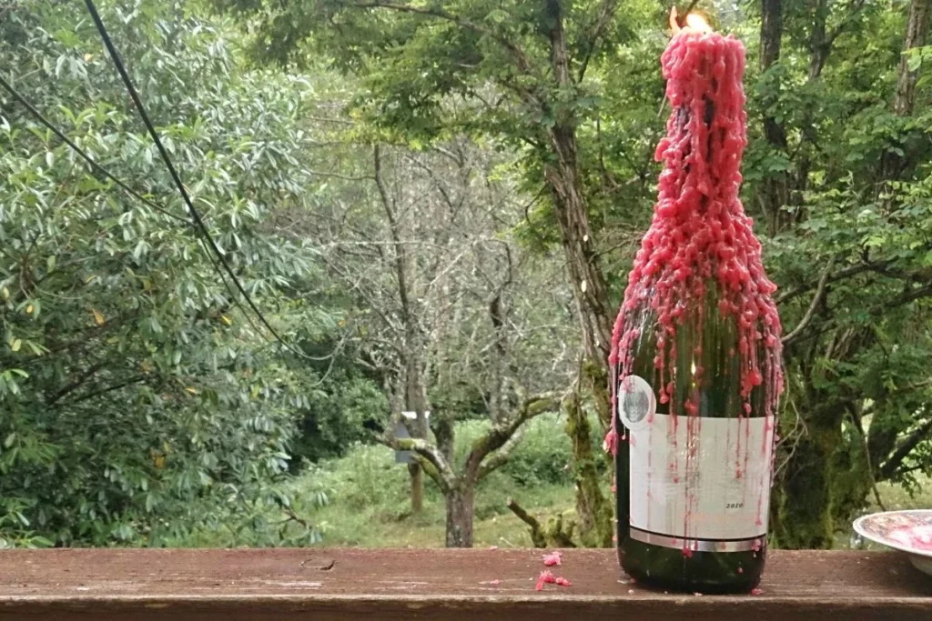 Empty green wine bottle reused as a candle holder with pink wax drips on an outdoor railing