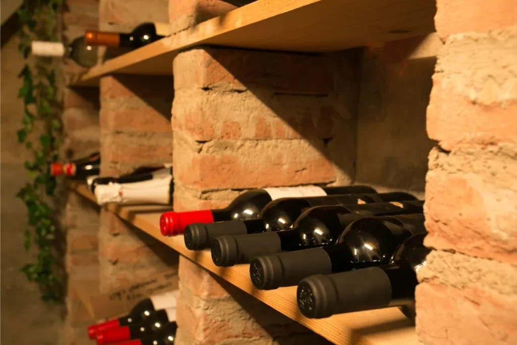 Wine bottles resting on their sides on wooden shelves in a dimly lit brick cellar