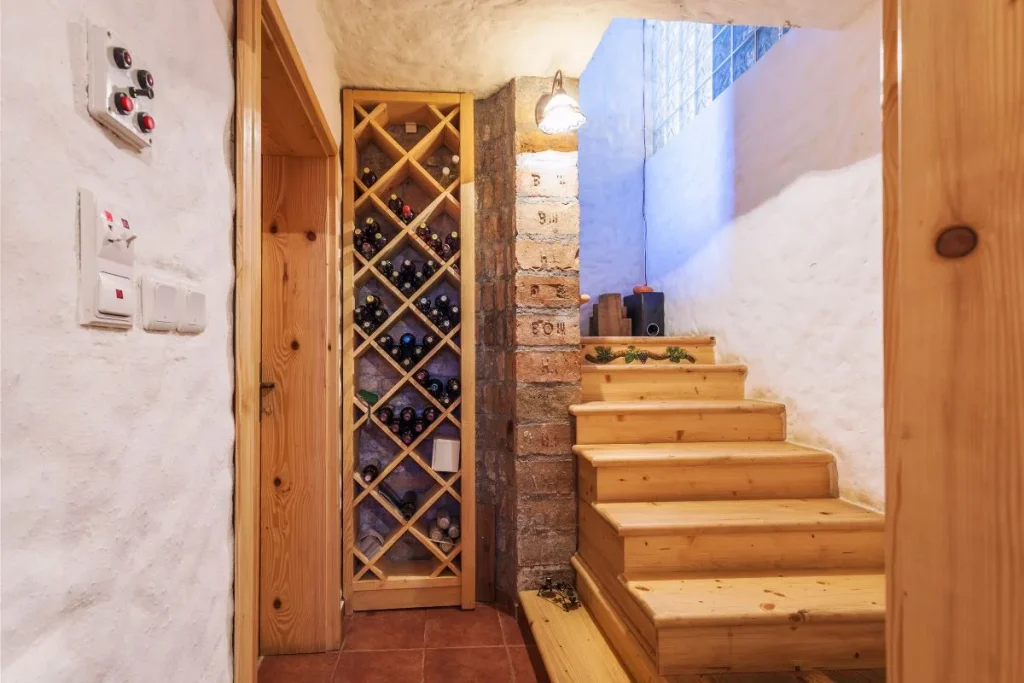 Built-in wooden diamond bin wine rack holding bottles beside pine stairs in a basement cellar
