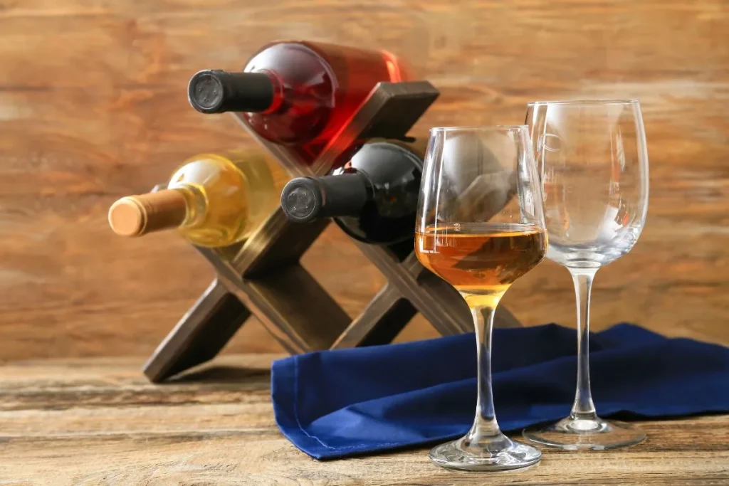 Three wine bottles resting neck down in a small wooden rack beside two glasses, one filled