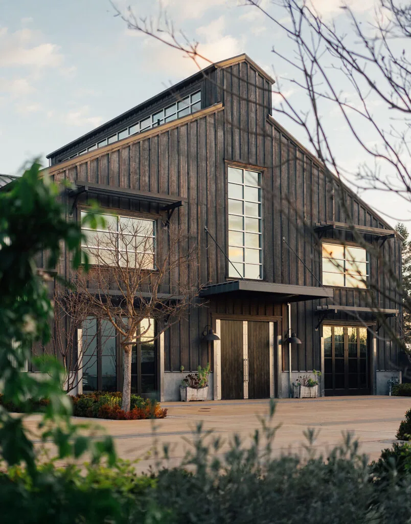 Modern barn style winery building with dark wood siding and tall windows at golden hour