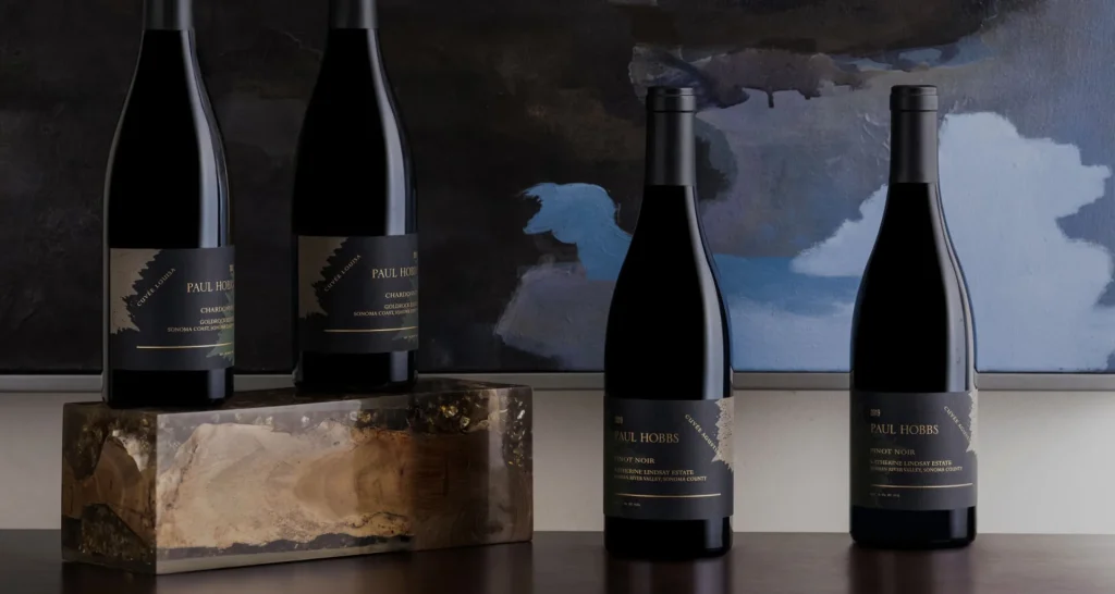 Four Paul Hobbs wine bottles displayed on a dark wood table in front of abstract artwork