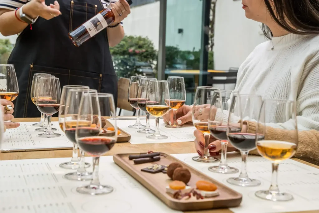 A host pouring amber Port for guests at a tasting table set with glasses and a chocolate board